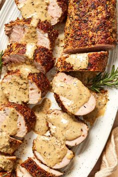 sliced pork with mustard sauce on a white platter next to rosemary sprigs