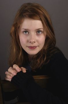 a woman with red hair and blue eyes posing for a photo in front of a gray background