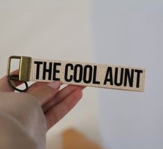 a hand holding a keychain with the word the cool aunt on it