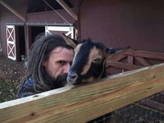 a man standing next to a goat on top of a wooden fence