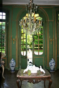 a room with green walls and chandelier in the center, surrounded by windows