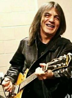 a man with long hair playing an electric guitar in a recording studio, smiling at the camera