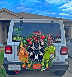 a christmas wreath on the back of a jeep parked in front of a house with two stuffed animals