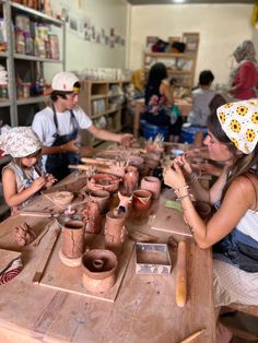 a group of people sitting around a wooden table with pottery on it's sides