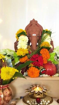 an elephant statue sitting on top of a wooden table next to flowers and fruit in vases