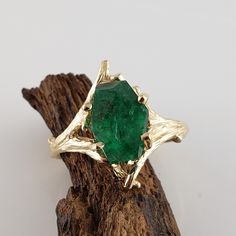 a green ring sitting on top of a piece of driftwood next to a tree branch