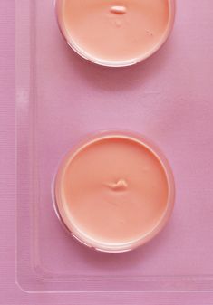 two jars of cream sitting on top of a plastic tray next to each other in front of a pink background