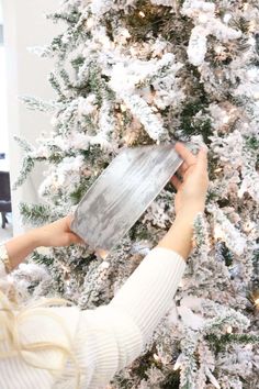 a woman is decorating a christmas tree with silver tinsel and white snowflakes