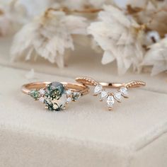 two rings with green and white stones on them sitting on a table next to flowers