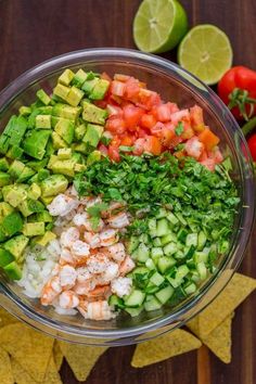 a bowl filled with shrimp, cucumber, tomatoes and cilantro next to tortilla chips