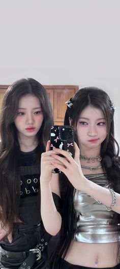 two young women taking a selfie in front of a mirror with their cell phones