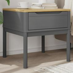 a nightstand with a book and coffee cup on it next to a plant in a white room