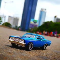 a blue toy car sitting on top of a road next to tall buildings in the background