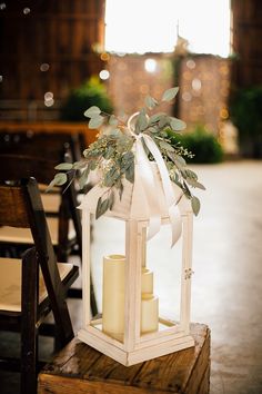 a white lantern with candles and greenery on the top sits in front of an empty chair