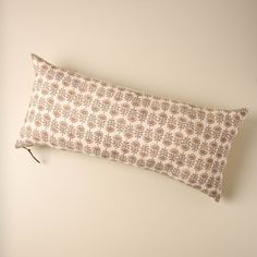 a decorative pillow on a white wall with a brown and tan flower pattern, hanging from a hook