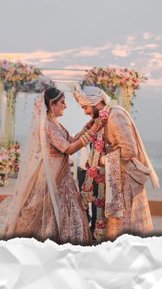 two people standing next to each other in front of an arch with flowers on it