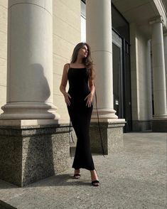 a woman in a black dress is standing on the sidewalk with her hand on her hip