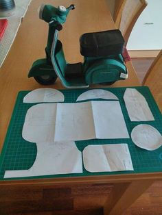 a motor scooter sitting on top of a table next to cut out pieces of paper