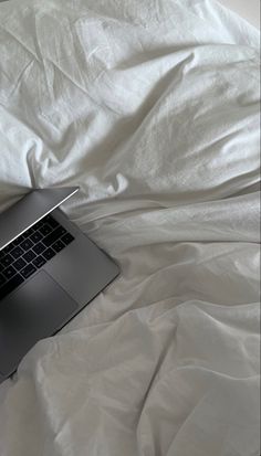 an open laptop computer sitting on top of a white sheeted bed cover covered in sheets