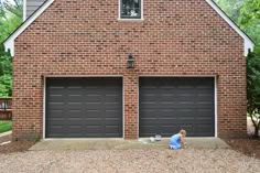 a little boy sitting on the ground in front of two garages with one door open