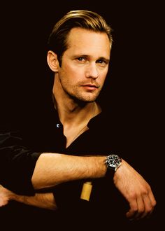 a man with a watch on his wrist looking at the camera while wearing a black shirt