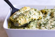 a white casserole dish with broccoli and cheese in it, being lifted by a spoon