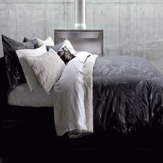 a bed with black and white comforters in front of a gray brick wall next to a window