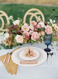 the table is set with plates, silverware and pink flowers on top of it