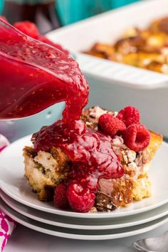 a person pouring raspberry sauce onto a piece of cake on a white plate