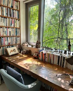 a desk with many books on it in front of a large window filled with trees