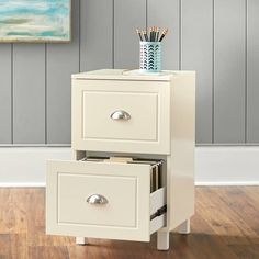 two drawers with pencils in them on a wooden floor next to a painting and wall