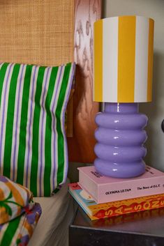 a purple lamp sitting on top of a stack of books next to a striped pillow