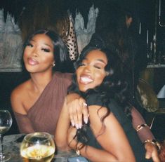 two women sitting at a table with wine glasses in front of them and one woman smiling