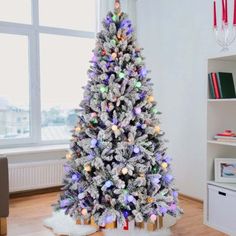 a white christmas tree with multicolored lights in a living room next to a window