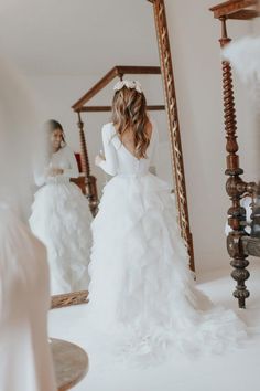 a woman in a white wedding dress looking at herself in the mirror