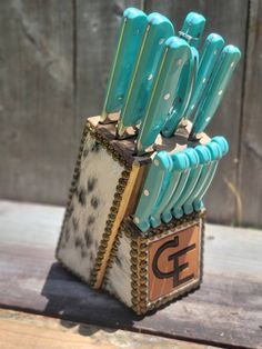 a bunch of blue knives are in a holder on a wooden table next to a fence