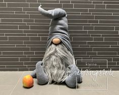 an odd looking stuffed animal laying on the ground next to two apples and a brick wall