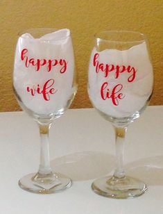 two wine glasses sitting on top of a table with happy life painted on the side