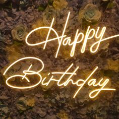 a neon sign that says happy birthday with flowers in the background