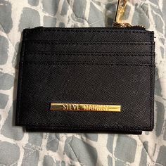 a black card case sitting on top of a bed next to a gold keychain