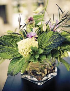 a vase filled with flowers and greenery on top of a table