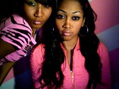 two beautiful young women standing next to each other in front of a pink and blue wall