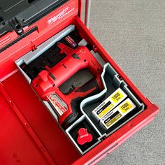 a red toolbox filled with tools on top of a gray carpeted flooring