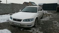 a white car parked in the snow next to a brick wall and fenced area