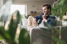 a man sitting on a couch in front of a potted plant and looking at the camera