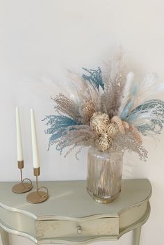 a vase filled with feathers sitting on top of a table next to two white candles