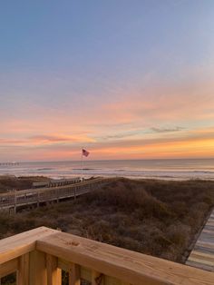 a wooden deck overlooks the beach and ocean at sunset with an american flag flying in the distance