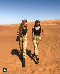 two women walking in the desert with sand dunes behind them