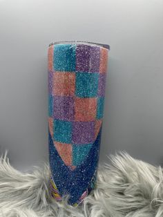 a purple and blue checkered tumbler cup sitting on top of a furry rug