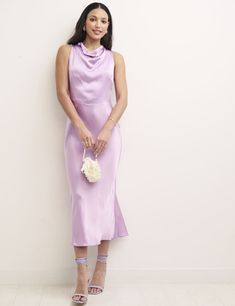 a woman standing in front of a wall wearing a purple dress and holding a white bouquet